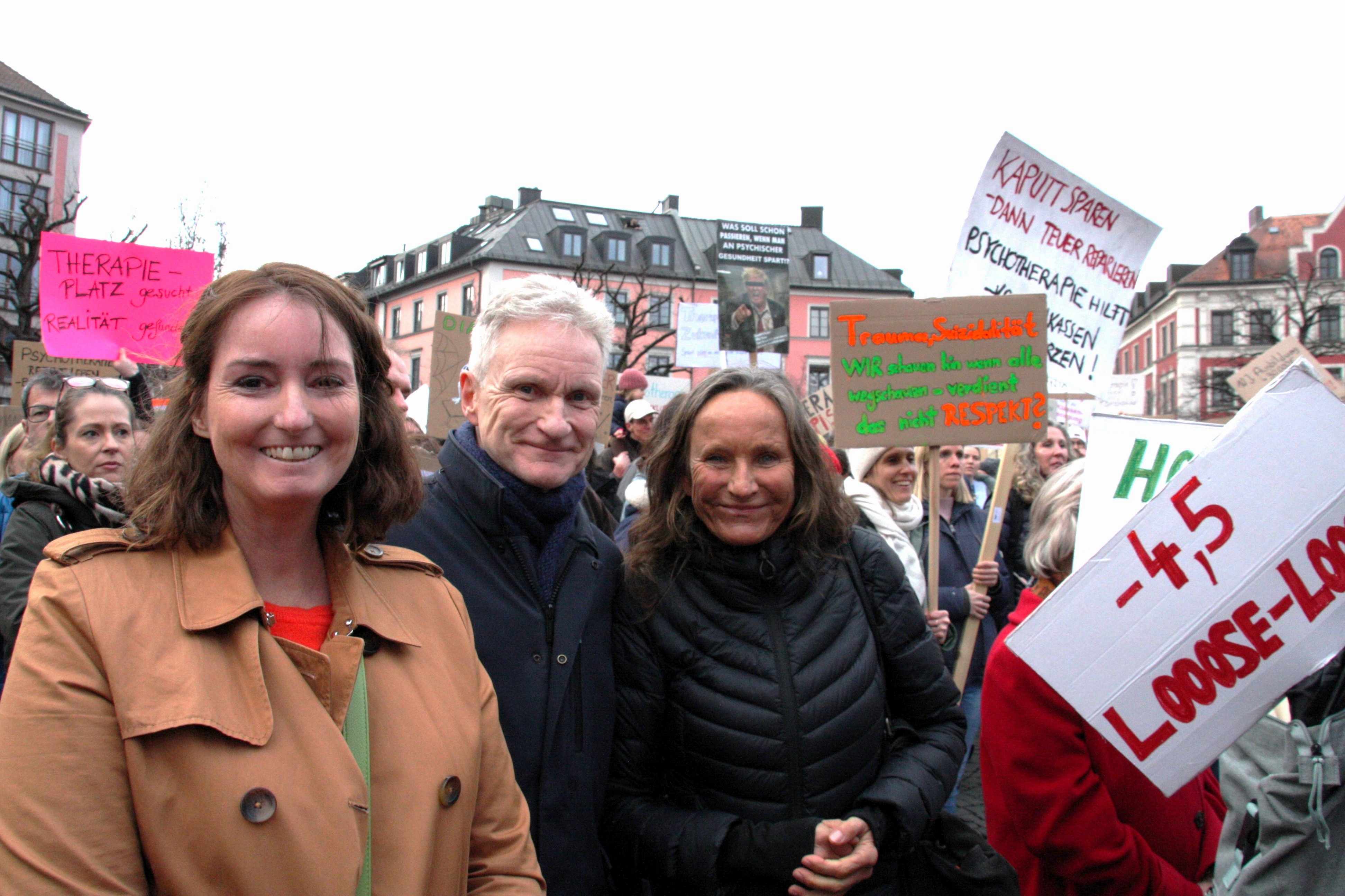 Zwei Frauen und ein Mann stehen in einer Gruppe von Demonstrierenden, die Plakate hochhalten